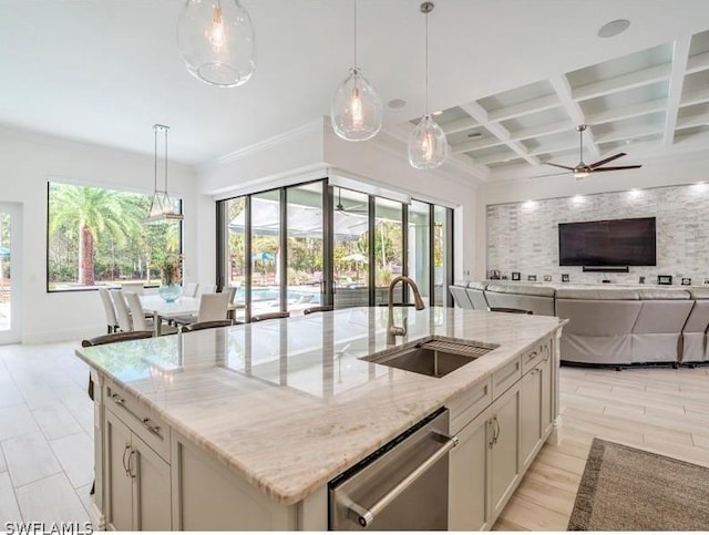 kitchen with coffered ceiling, sink, stainless steel dishwasher, light stone countertops, and an island with sink