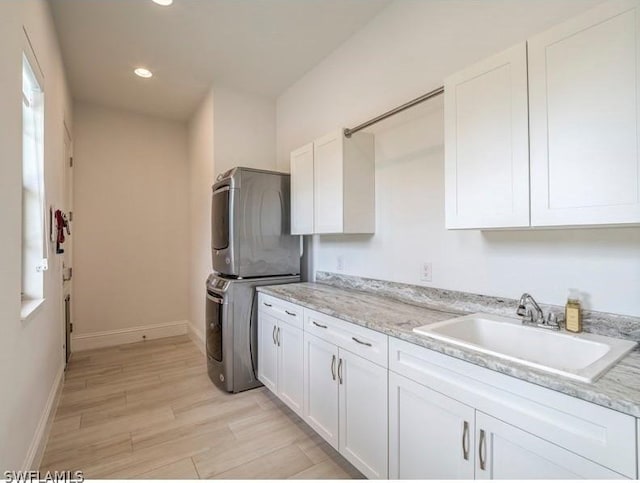 kitchen with white cabinetry, sink, light stone countertops, and stacked washer and clothes dryer