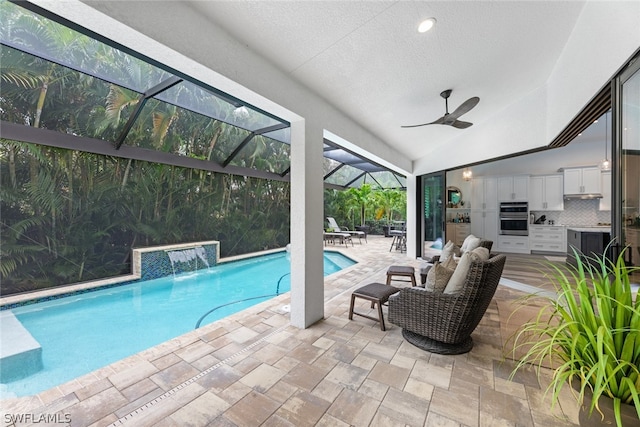 view of pool featuring pool water feature, ceiling fan, a patio, a lanai, and an outdoor kitchen