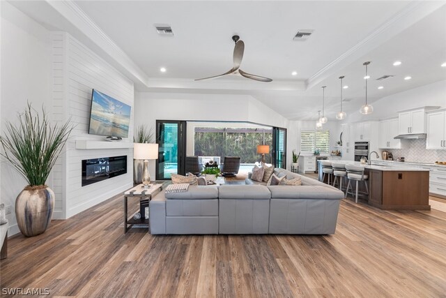 living room with ceiling fan, hardwood / wood-style floors, sink, and a tray ceiling