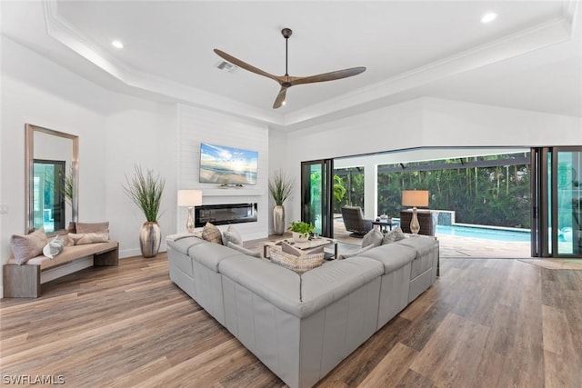 living area with a glass covered fireplace, light wood finished floors, a raised ceiling, and visible vents