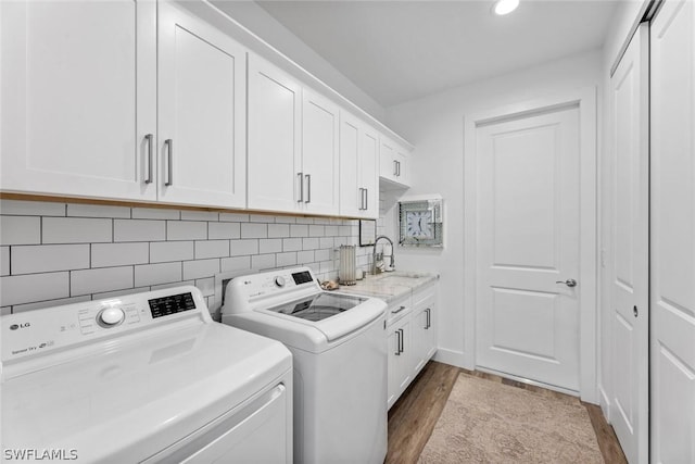 laundry room featuring washing machine and dryer, cabinet space, a sink, and wood finished floors