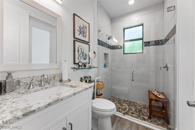 bathroom featuring toilet, a stall shower, wood finished floors, and vanity