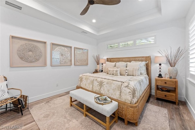 bedroom with baseboards, visible vents, a raised ceiling, and wood finished floors