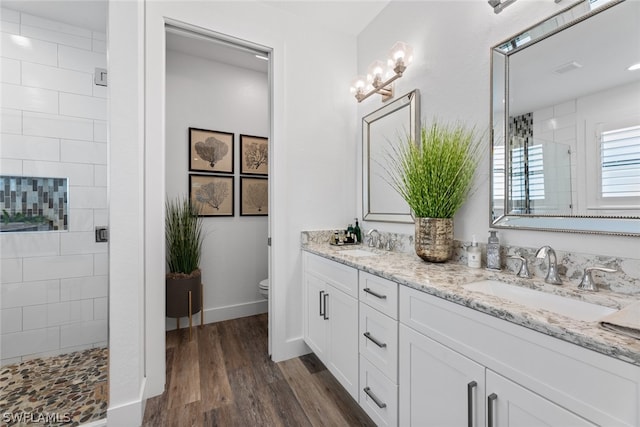 bathroom featuring double vanity, wood-type flooring, toilet, and tiled shower