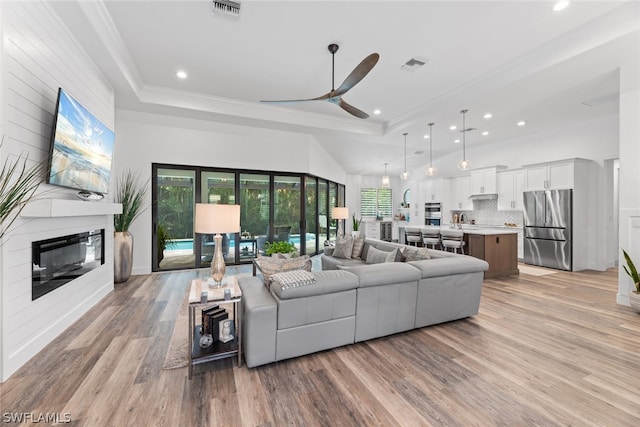 living room featuring a raised ceiling, plenty of natural light, ceiling fan, and light wood-type flooring