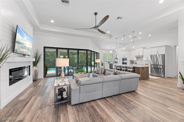 living area featuring light wood finished floors, a fireplace, visible vents, and crown molding