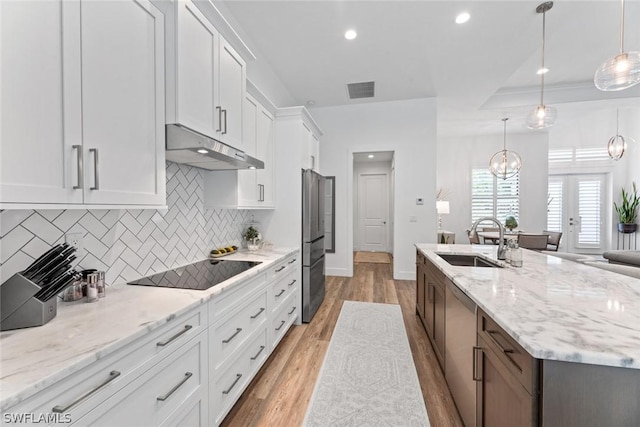 kitchen with light wood finished floors, white cabinetry, a sink, under cabinet range hood, and black electric cooktop