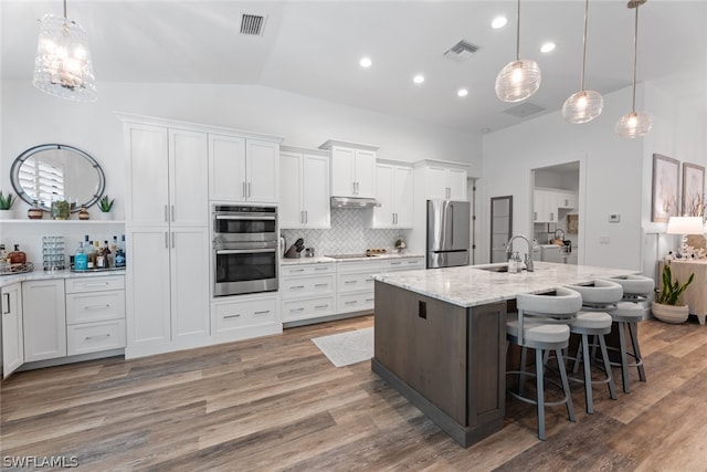 kitchen with decorative backsplash, wood-type flooring, white cabinets, and stainless steel appliances