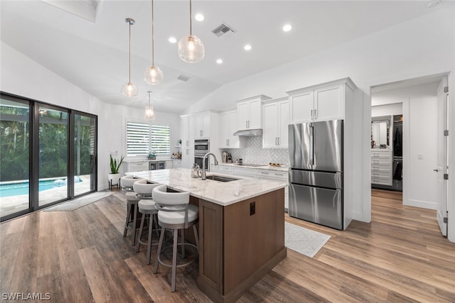 kitchen featuring hardwood / wood-style flooring, a center island with sink, appliances with stainless steel finishes, lofted ceiling, and backsplash