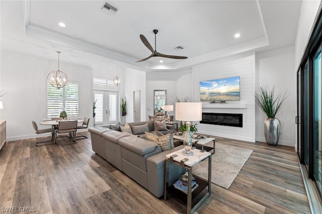 living room featuring a glass covered fireplace, visible vents, baseboards, a raised ceiling, and dark wood finished floors