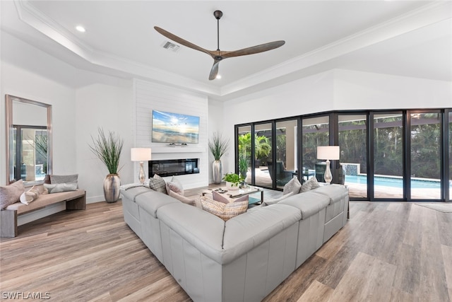 living room with a tray ceiling, light wood-type flooring, and ceiling fan