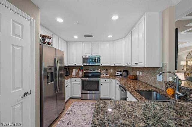 kitchen with sink, tasteful backsplash, dark stone countertops, stainless steel appliances, and white cabinets