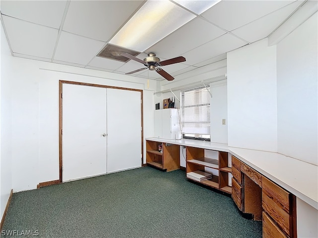 home office with a paneled ceiling, dark carpet, and ceiling fan