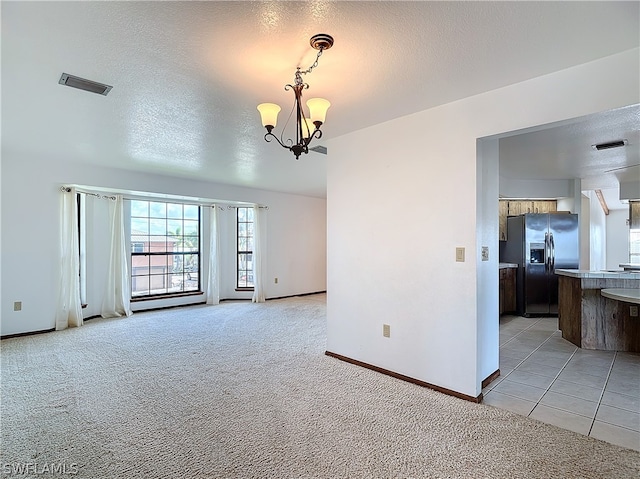 carpeted spare room featuring an inviting chandelier and a textured ceiling