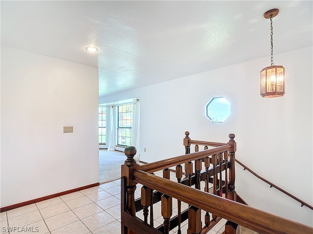 hall with an inviting chandelier, a textured ceiling, and light tile patterned flooring