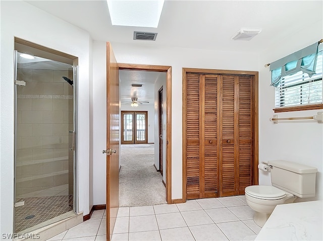 bathroom with ceiling fan, toilet, a shower with shower door, a skylight, and tile patterned flooring