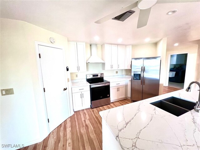 kitchen featuring white cabinets, appliances with stainless steel finishes, light hardwood / wood-style flooring, wall chimney exhaust hood, and sink