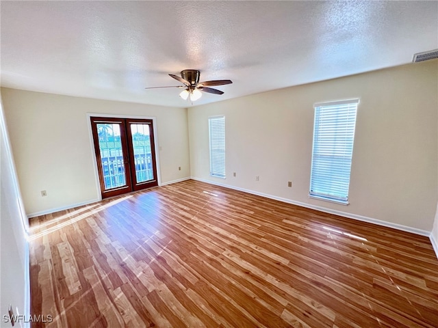 empty room featuring a textured ceiling, hardwood / wood-style flooring, french doors, and ceiling fan