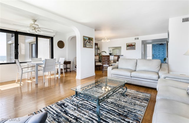 living room with arched walkways, hardwood / wood-style floors, ceiling fan with notable chandelier, and baseboards