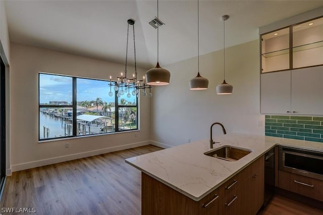 kitchen featuring a water view, backsplash, a sink, light stone countertops, and dishwasher