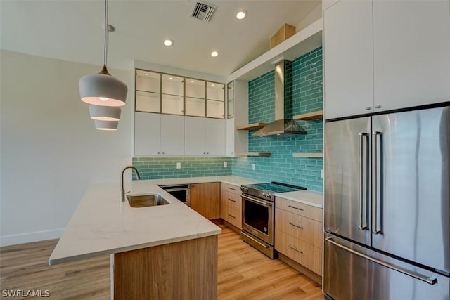 kitchen with white cabinets, wall chimney exhaust hood, hanging light fixtures, stainless steel appliances, and a sink