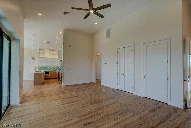 unfurnished bedroom with sink, a towering ceiling, light hardwood / wood-style floors, and two closets