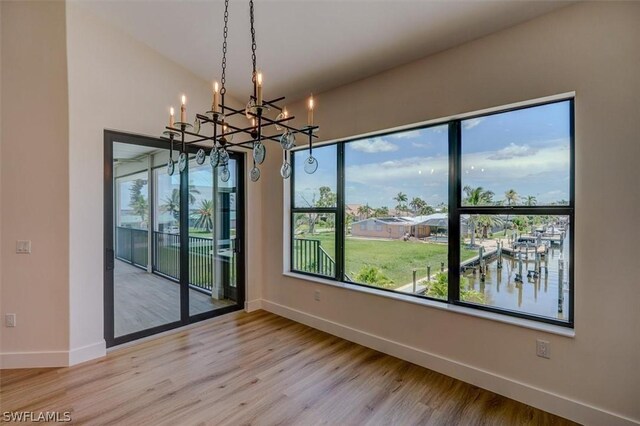 unfurnished dining area with wood-type flooring, vaulted ceiling, a water view, and an inviting chandelier