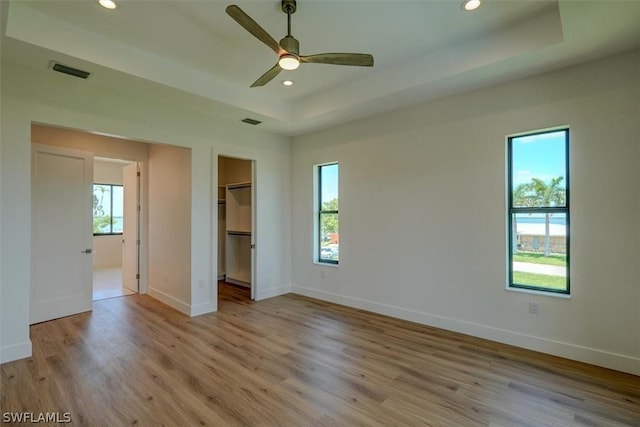 unfurnished bedroom featuring a raised ceiling, a walk in closet, ceiling fan, light hardwood / wood-style floors, and a closet