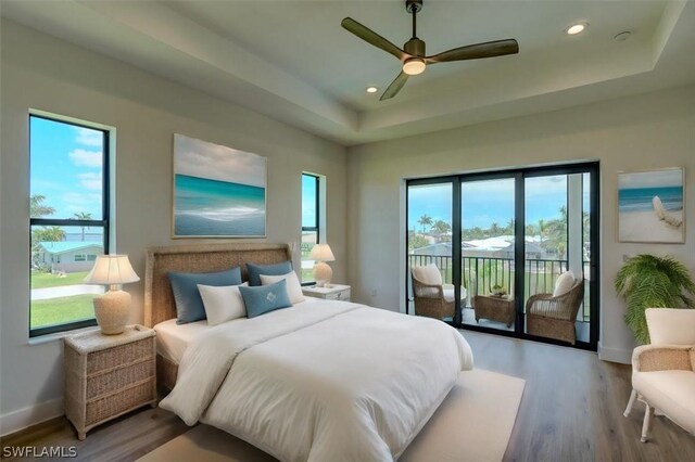 bedroom featuring hardwood / wood-style floors, access to outside, ceiling fan, and a tray ceiling