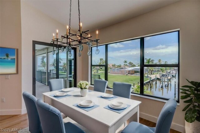 dining area with light wood-type flooring, a water view, and a notable chandelier