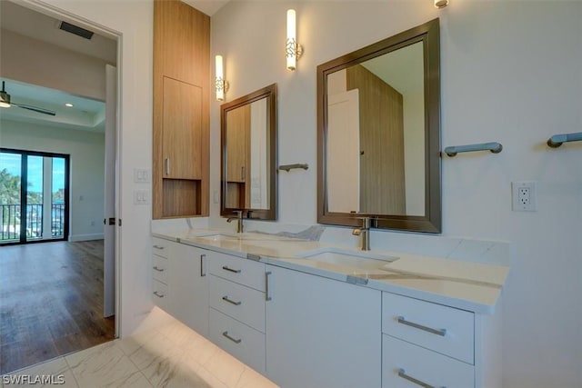 full bath featuring ceiling fan, double vanity, a sink, and a raised ceiling