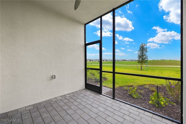 unfurnished sunroom featuring ceiling fan and a rural view