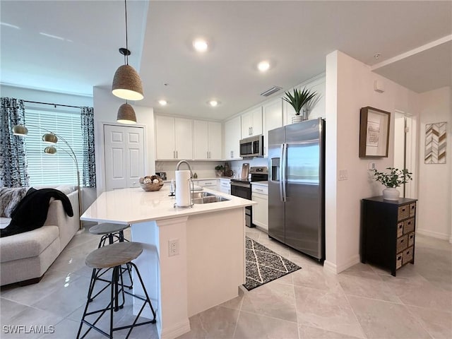 kitchen featuring a kitchen bar, sink, stainless steel appliances, white cabinets, and hanging light fixtures