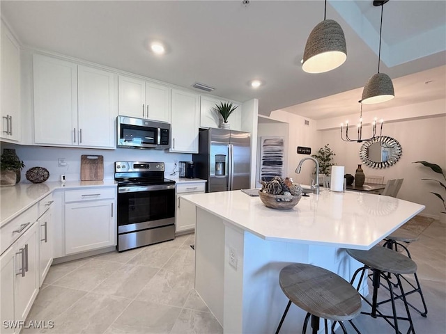 kitchen featuring appliances with stainless steel finishes, a breakfast bar area, decorative light fixtures, white cabinetry, and a kitchen island with sink