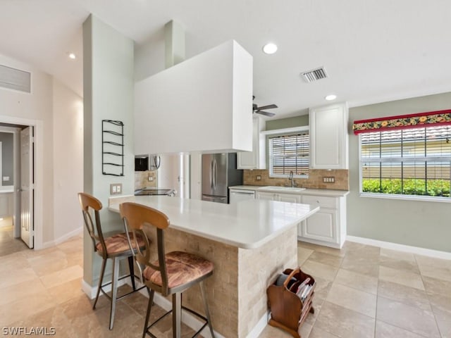 kitchen with white cabinets, a kitchen breakfast bar, sink, ceiling fan, and stainless steel fridge