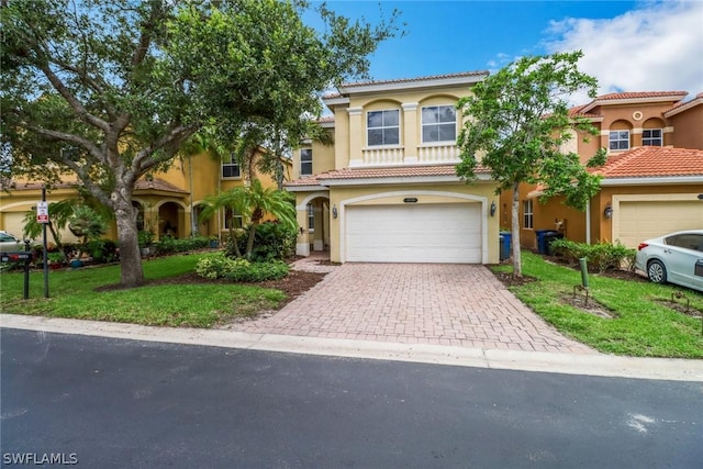 mediterranean / spanish home featuring stucco siding, a tiled roof, an attached garage, decorative driveway, and a front yard