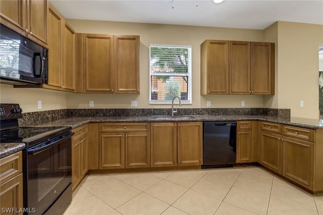 kitchen featuring light tile patterned flooring, a sink, brown cabinets, black appliances, and dark stone countertops