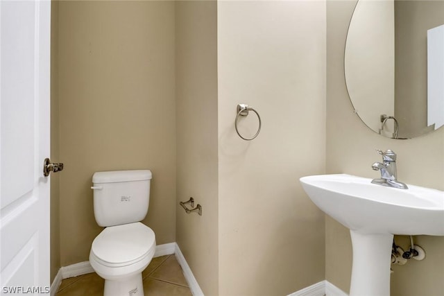 half bathroom with toilet, baseboards, a sink, and tile patterned floors