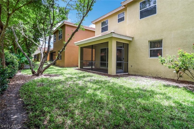 back of property with a lawn, a sunroom, and stucco siding