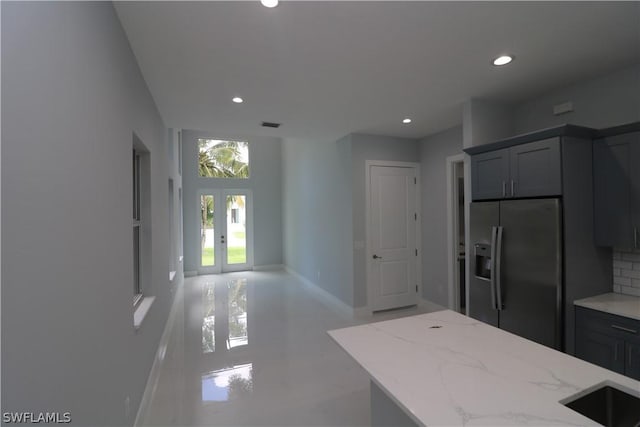 kitchen with gray cabinetry, light stone countertops, french doors, stainless steel fridge, and decorative backsplash