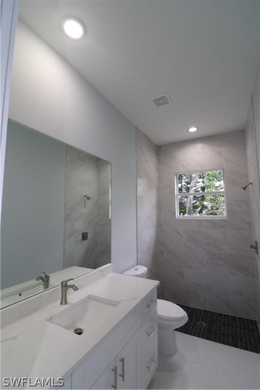 bathroom with a tile shower, vanity, toilet, and tile patterned floors