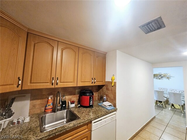 kitchen featuring dark stone counters, light tile patterned flooring, decorative backsplash, sink, and white dishwasher