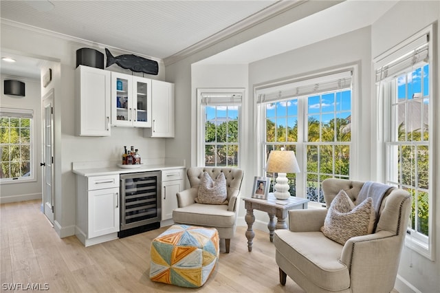 sitting room with ornamental molding, beverage cooler, indoor bar, and light wood-type flooring