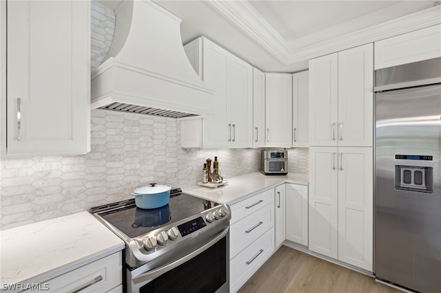 kitchen featuring premium range hood, tasteful backsplash, white cabinets, and appliances with stainless steel finishes