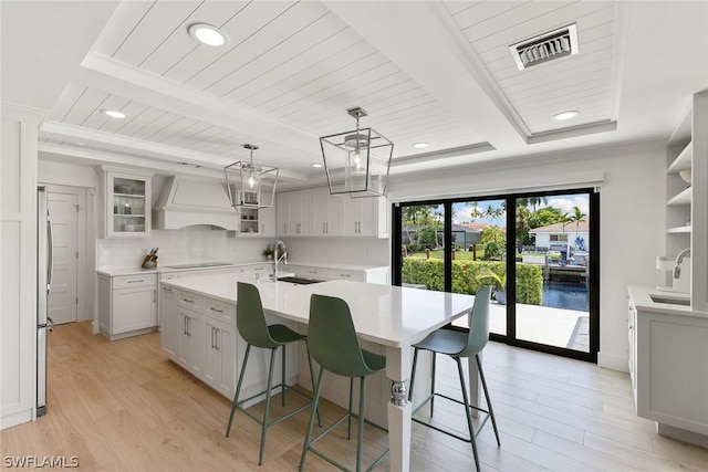 kitchen with hanging light fixtures, white cabinets, an island with sink, a water view, and custom exhaust hood