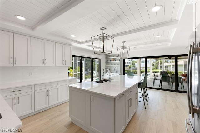 kitchen with light wood-type flooring, a center island with sink, hanging light fixtures, and sink