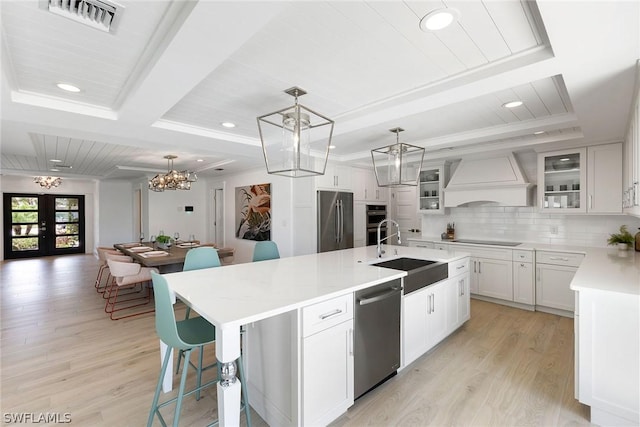 kitchen with sink, custom range hood, an island with sink, and appliances with stainless steel finishes