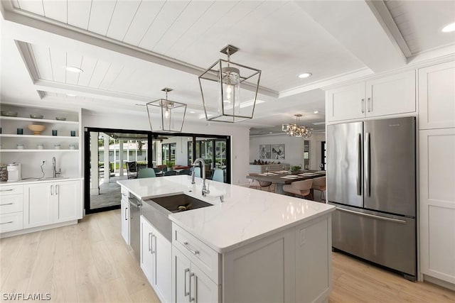 kitchen featuring stainless steel refrigerator, an island with sink, white cabinets, and hanging light fixtures