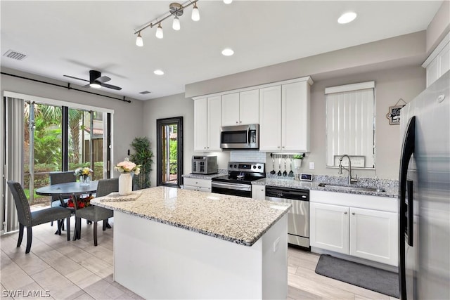 kitchen featuring ceiling fan, a kitchen island, white cabinetry, and stainless steel appliances